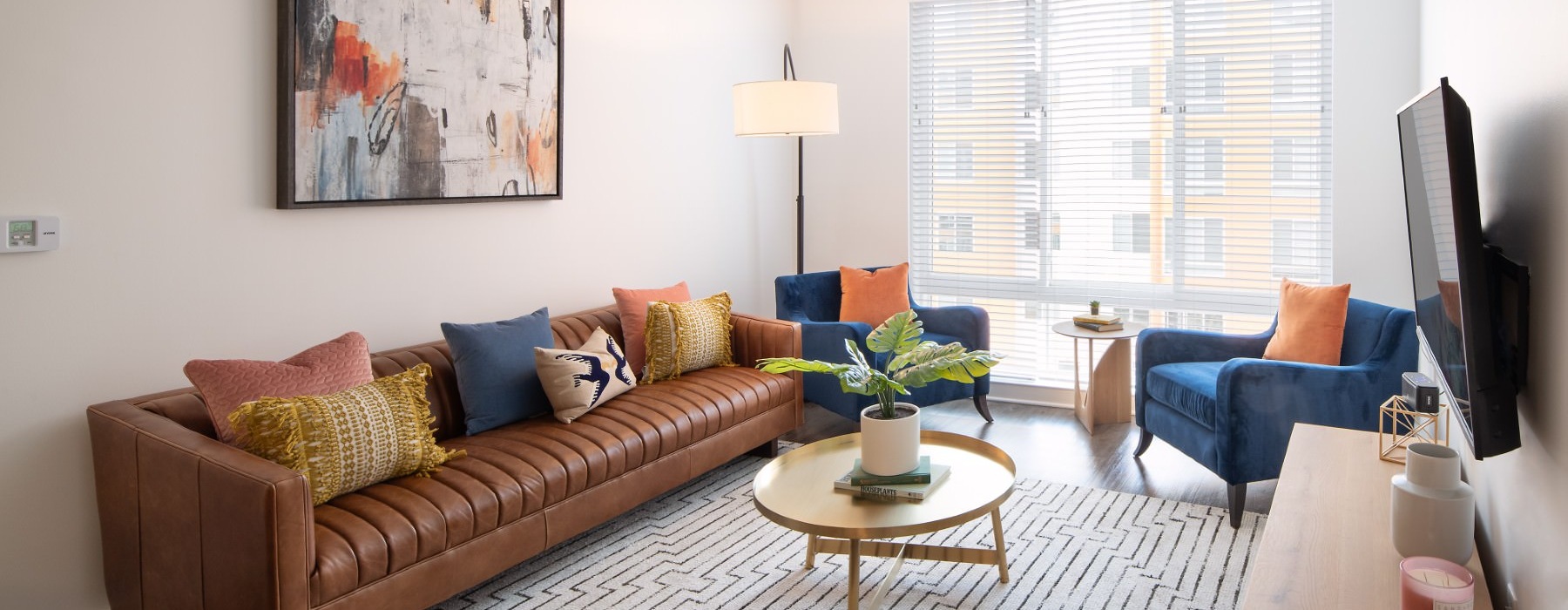 a living room with a couch, tv, chairs, tables and a window